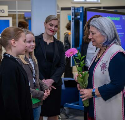 La gouverneure générale Mary Simon tient une fleur rose et s’adresse à deux écoliers. Deux femmes se tiennent derrière eux.