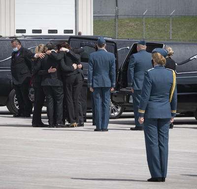 Family members of the deceased embrace each other beside a hearse.