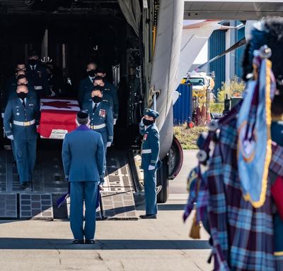 Le cercueil de la capitaine Jennifer Casey est transporté hors de l'avion par des membres des Forces armées canadiennes. Un joueur de cornemuse est au premier plan de la photo. 