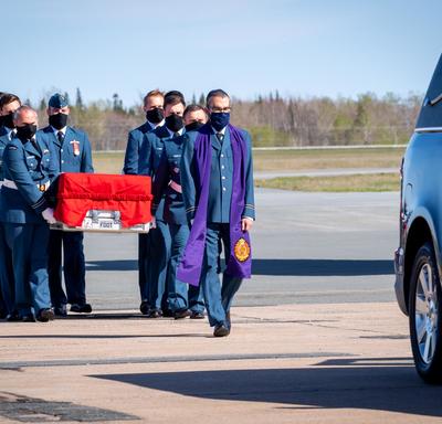 Le cercueil de la capitaine Jennifer Casey est transporté par des membres des forces armées canadiennes vers le corbillard. Le chapelain est devant le cercueil,