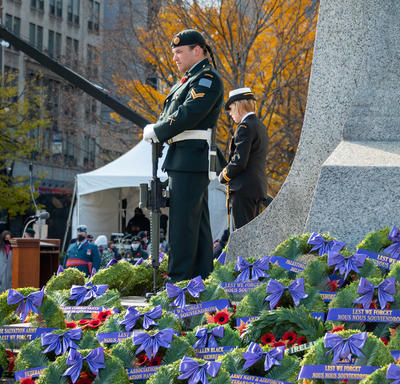 Sentries are positioned by the National War Memorial and surrounded by wreaths during the National Remembrance Day ceremony. One sentry is wearing a Canadian Army uniform, and the other is wearing a Royal Canadian Navy uniform.