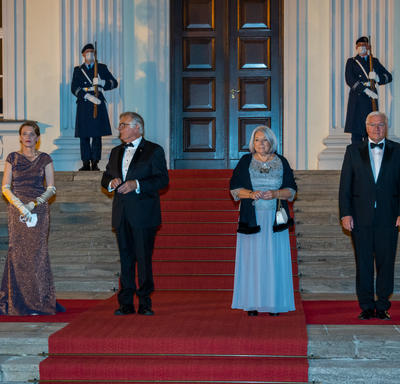Their Excellencies stand on the red carpet with two other people in formal evening attire at the entrance to a building.