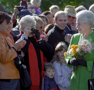  The Queen, holding bouquets of flowers and wearing a green coat, greets a crowd of people outside Rideau Hall.