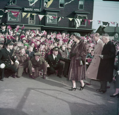 La princesse Elizabeth, qui porte un long manteau de fourrure, passe devant une foule. Plusieurs photographes sont à genoux devant elle pour prendre des photos.