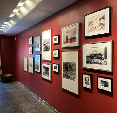 Vue en angle à droite d'un mur rouge qui présente un mélange de 17 photographies, croquis et peintures sur un mur rouge.
