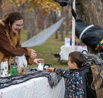 A child is looking at a Halloween decorating table. A member of the Rideau Hall staff is holding a small jar.