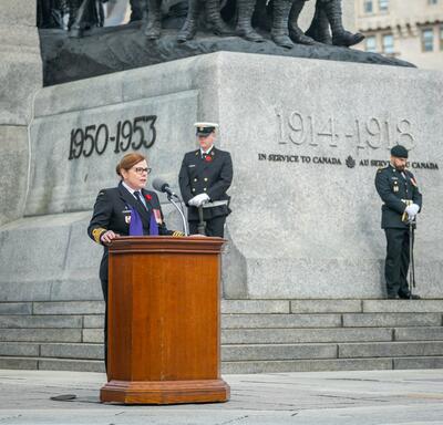 Un padre militaire s'exprime sur un pupitre devant le Monument commémoratif de guerre du Canada.