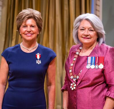La gouverneure générale Simon se tient à côté d’une femme qui porte une médaille épinglée à sa robe bleue..