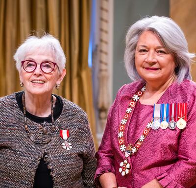 La gouverneure générale Simon se tient à côté d’une femme qui porte une médaille épinglée à son cardigan brun.