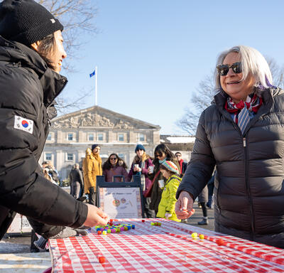 La gouverneure générale Mary Simon parle à une personne debout derrière une table où se trouve un jeu coloré. Ils sont à l’extérieur et portent des vêtements d’hiver.