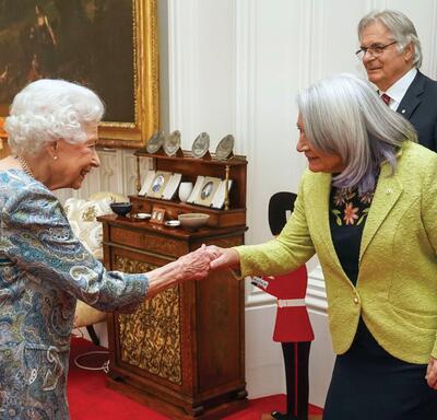 La gouverneure générale Mary Simon serre la main de la reine Elizabeth II. M. Whit Fraser sourit et se tient derrière elles.