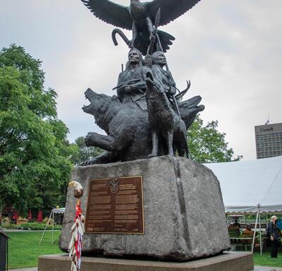 A close-up of the National Aboriginal Veterans Monument. Two of the figures hold weapons, and two hold spiritual objects. An eagle occupies the highest point of the sculpture. There is also a wolf, grizzly, buffalo and caribou.