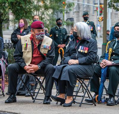La gouverneure générale Mary Simon est assise à l’extérieur et parle avec un ancien combattant autochtone.