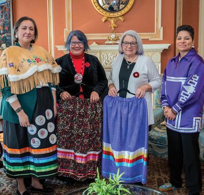La gouverneure générale Mary Simon est debout à côté de trois femmes : la cheffe nationale Archibald, la grande cheffe Kahsennenhawe Sky-Deer et la grande cheffe Gull-Masty
