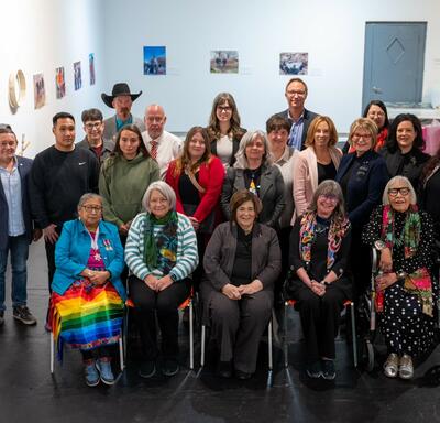 Un groupe diversifié de 21 personnes pose à l'intérieur, souriant. Certaines sont assises, d'autres debout, entourées d'œuvres d'art accrochées aux murs