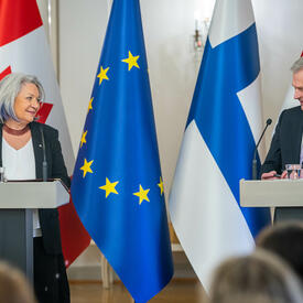 La gouverneure générale Mary Simon et le président Sauli Niinistö sont debout derrière un pupitre. Derrière eux se trouvent, de gauche à droite, le drapeau du Canada, le drapeau de la Finlande et le drapeau de l’Union européenne.