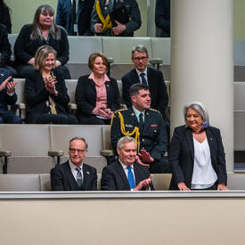 La gouverneure générale Mary Simon est debout sur un balcon du parlement finlandais. Plusieurs parlementaires sont assis autour d’elle. Ils applaudissent.