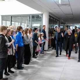 La gouverneure générale Mary Simon marche dans un bâtiment devant des étudiants. Quelques personnes marchent derrière elle. Les étudiants tiennent des drapeaux de la Finlande et du Canada. 
