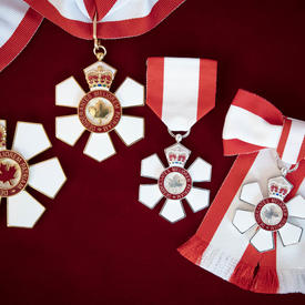 Quatre médailles représentant les trois niveaux de l'Ordre du Canada sont représentées sur un fond de velours rouge.