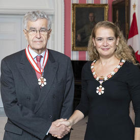 La gouverneure générale, Julie Payette, se tient debout aux côtés de Louis Lebel.  Tous deux portent l'insigne de l'Ordre du Canada.