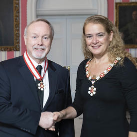 La gouverneure générale, Julie Payette, se tient debout aux côtés de Terence Matthews.  Tous deux portent l'insigne de l'Ordre du Canada.