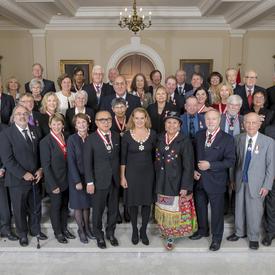La Gouverneure générale, Julie Payette, est entourée de 41 récipiendaires de l'Ordre du Canada.  Ils se tiennent debout dans l'escalier du foyer de Rideau Hall. 