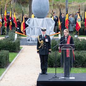 La gouverneure générale du Canada prend la parole à une tribune, avec sa femme aide-de-camp à sa droite. Derrière elle se trouve une sculpture géante en béton en forme de larme.