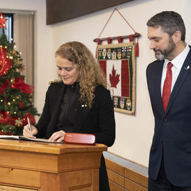 La gouverneure générale signe un livre d'or.  Sandy Silver, premier ministre du Yukon, se tient à ses côtés.