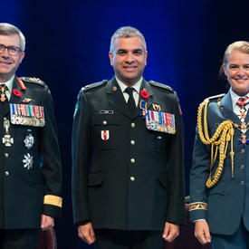 Le major Trevor Jain se tient entre le Vice-chef d'état-major de la Défense, le Lieutenant-général Paul Wynnyk (à   gauche) et Son Excellence la très honorable Julie Payette (à droite).