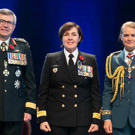 Le capitaine de vaisseau Rebecca Louise Patterson se tient entre le Vice-chef d'état-major de la Défense, le   Lieutenant-général Paul Wynnyk (à gauche) et Son Excellence la très honorable Julie Payette (à droite).