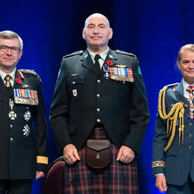  Le major James Edward Rene MacInnis se tient entre le Vice-chef d'état-major de la Défense, le Lieutenant-général   Paul Wynnyk (à gauche) et Son Excellence la très honorable Julie Payette (à droite)