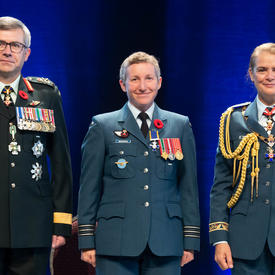 Le major Jennifer Lynn Morrison se tient entre le Vice-chef d'état-major de la Défense, le Lieutenant-général Paul   Wynnyk (à gauche) et Son Excellence la très honorable Julie Payette (à droite).