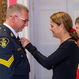 La gouverneure générale épingle une médaille sur la poitrine d'un récipiendaire de l'Ordre du mérite des corps policiers.