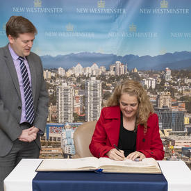 La gouverneure générale signe le livre d'or de la ville pendant que le maire se trouve à ses côtés.