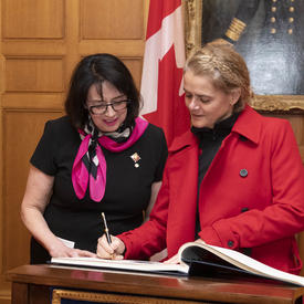 La gouverneure générale signe un livre d'or et Son Honneur l'honorable Janet Austin, lieutenante-gouverneure de la Colombie-Britannique, se tient à ses côtés.