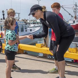 La gouverneure générale rencontre et serre la main d'une jeune fille dans le port de l'île d'Entrée.