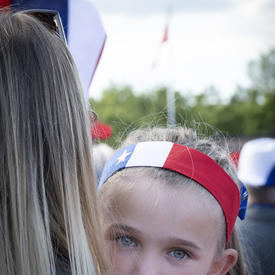 Une jeune fille vêtue des couleurs nationales acadiennes est dans les bras de sa mère. 