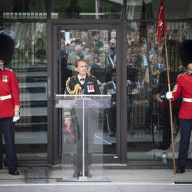 La gouverneure générale prononce une allocution à une tribune, deux gardes de cérémonie se tiennent solennellement de chaque côté.