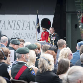 Le Chef d'état-major de la Défense prononce une allocution à une tribune, deux gardes de cérémonie se tiennent solennellement de chaque côté.