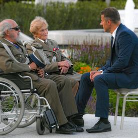 Photo d'un homme en costume parlant avec deux anciens combattants polonais en fauteuil roulant.