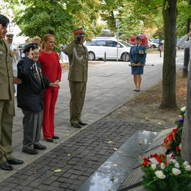 Deux officiers polonais et un ancien combattant polonais saluent un monument aux côtés de la gouverneure générale.