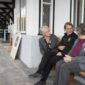 La gouverneure générale est assise avec deux femmes à l'extérieur du Cranberry Portage Heritage Museum.