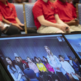 Une photo d'élèves assis dans la salle de la tente de Rideau Hall, avec une salle de classe virtuelle de Vancouver sur un écran.