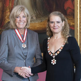 La gouverneure générale serre la main de Sally Wishart Armstrong.  Tous deux portent l'insigne de l'Ordre du Canada. 
