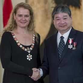 Yiyan Wu se tient à côté de la Gouverneure générale.  Tous deux sourient à la caméra.  Ils portent leur insigne de l'Ordre du Canada.
