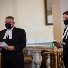 Deux personnes, toutes deux portant une tenue noire avec un col blanc, tiennent des documents.