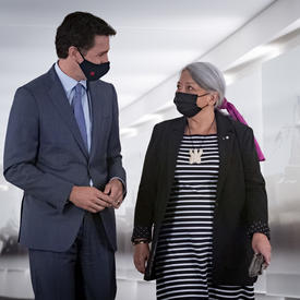 Le premier ministre Justin Trudeau et la gouverneure générale désignée Mary May Simon marchent dans un couloir côte à côte en se regardant.