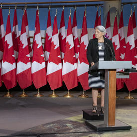 Le premier ministre Justin Trudeau et la gouverneure générale désignée Mary May Simon se tiennent chacun face à un podium devant plusieurs drapeaux du Canada derrière eux.
