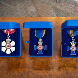 Trois décorations canadiennes de l'ordre national sont placées sur une table en bois dans des boîtes individuelles en daim bleu. La première décoration est rouge et blanche avec un ruban rouge et blanc. Les deuxième et troisième décorations sont bleues.