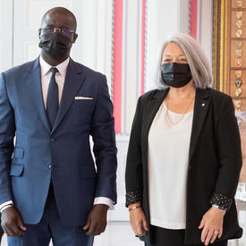 Un homme en costume et portant un masque se tient à la droite de la gouverneure générale Mary May Simon pour la prise d’une photo.